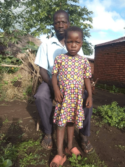 A pastor seated outside with a young child standing in front of him.